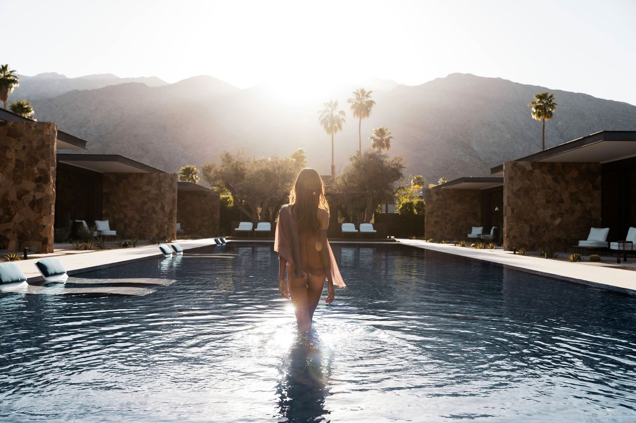 A woman wades in our pool beneath mountains and palm trees at our California boutique resort.